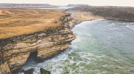 Coastal cliffs of Dhofar with waves crashing below and a red 4x4 parked on the edge near Salalah, Samhan mountain