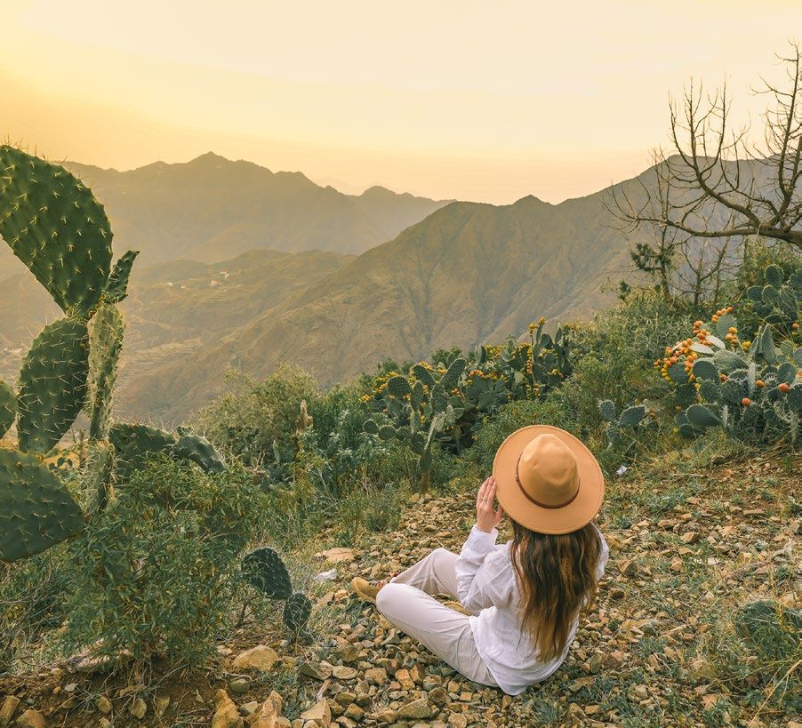 Author Iwona Deren sitting among cactus plants watching the sunset over the UAE mountains.