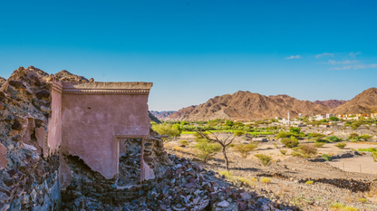 Ancient village ruins with desert mountains and a small oasis town in the background.