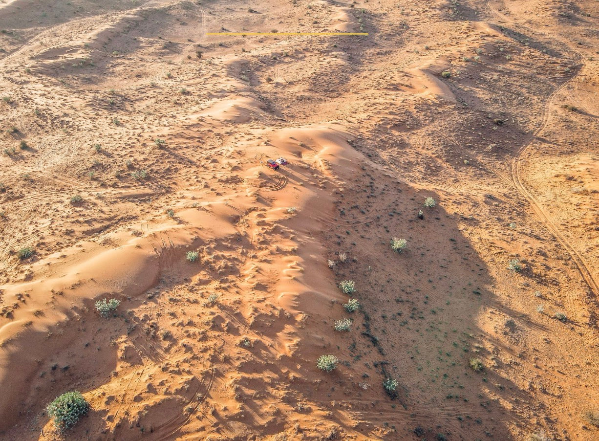Aerial view of golden sand dunes with a 4x4 vehicle driving through the Empty Quarter desert of the UAE.