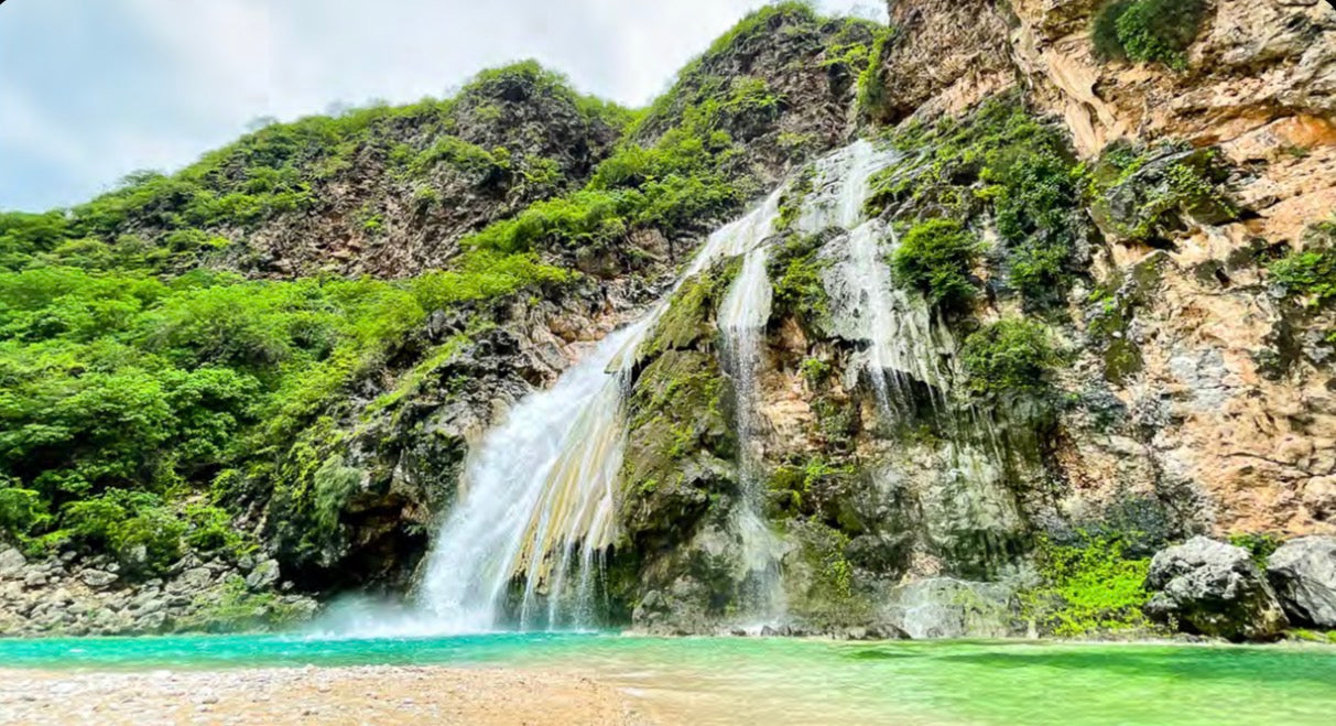 Ayn Khor waterfall cascading into turquoise water during Khareef season in Salalah