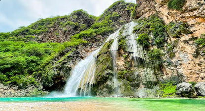 Ayn Khor waterfall cascading into turquoise water during Khareef season in Salalah
